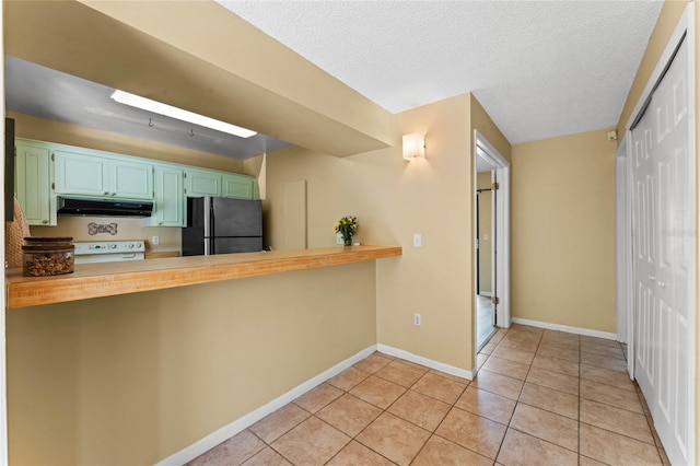 kitchen with baseboards, light tile patterned flooring, freestanding refrigerator, stove, and under cabinet range hood