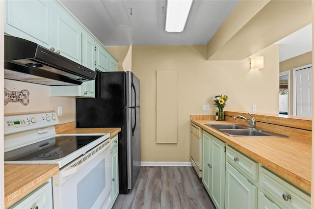 kitchen featuring light wood finished floors, green cabinets, under cabinet range hood, white appliances, and a sink