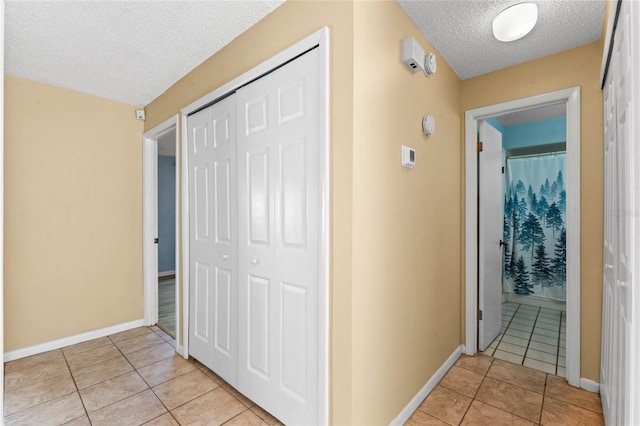 hallway featuring light tile patterned floors, a textured ceiling, and baseboards