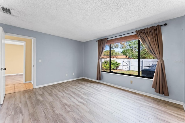 empty room with visible vents, a textured ceiling, baseboards, and wood finished floors