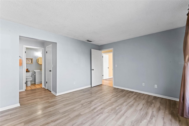 unfurnished bedroom featuring light wood finished floors, visible vents, baseboards, ensuite bathroom, and a textured ceiling