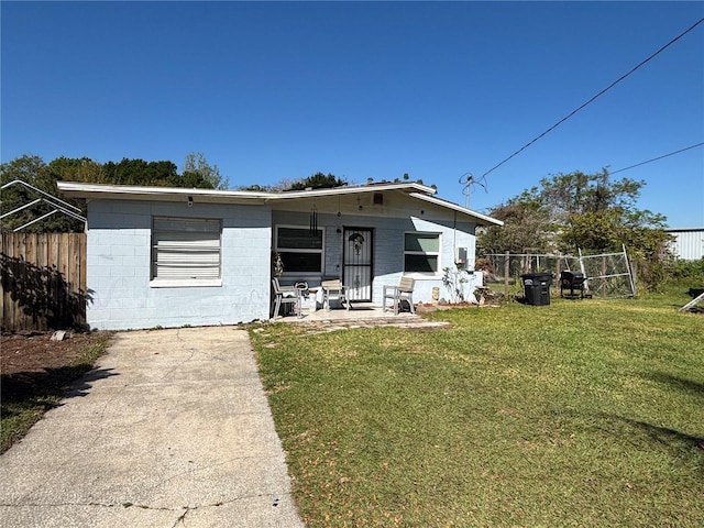 view of front of home with concrete block siding, a front lawn, fence, and a patio area