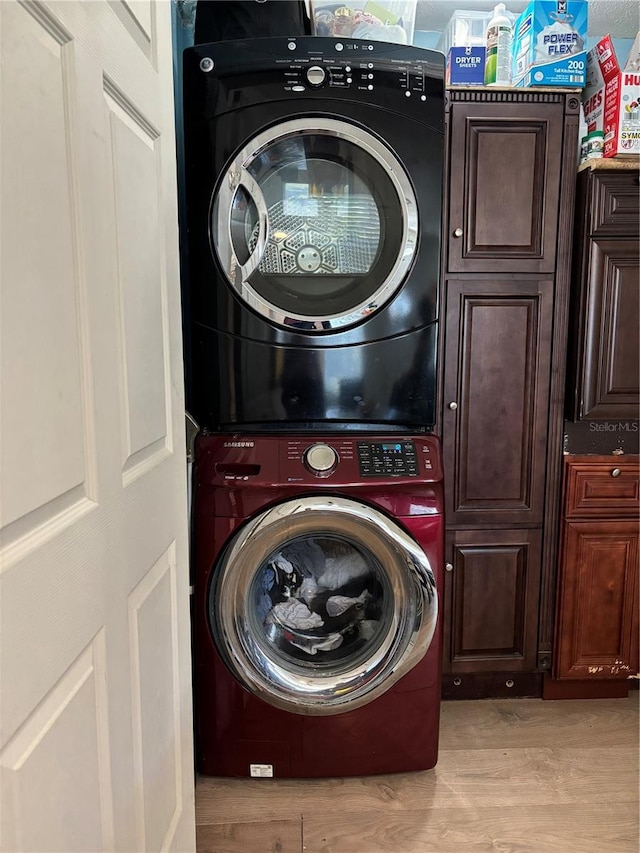 laundry room featuring cabinet space, stacked washer / drying machine, and light wood-type flooring