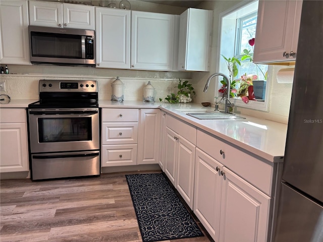 kitchen featuring white cabinets, appliances with stainless steel finishes, light countertops, and a sink