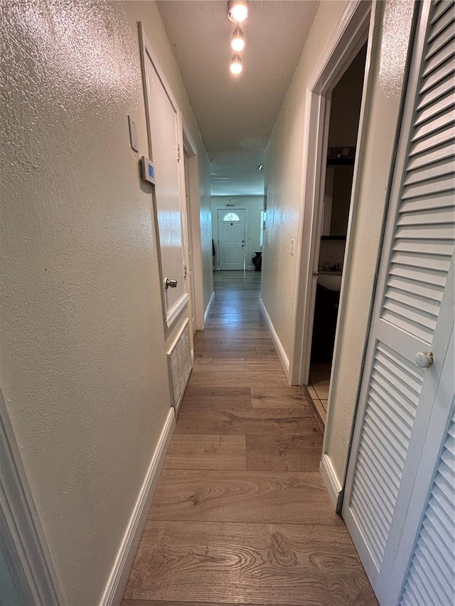 hall with baseboards, wood finished floors, and a textured wall