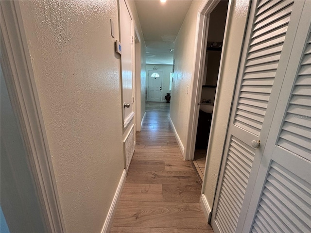 corridor featuring baseboards, a textured wall, and wood finished floors