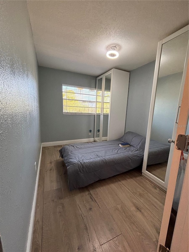 unfurnished bedroom with a textured wall, a textured ceiling, baseboards, and wood finished floors