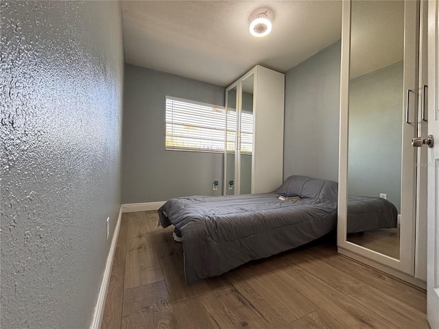 bedroom featuring wood finished floors, baseboards, and a textured wall