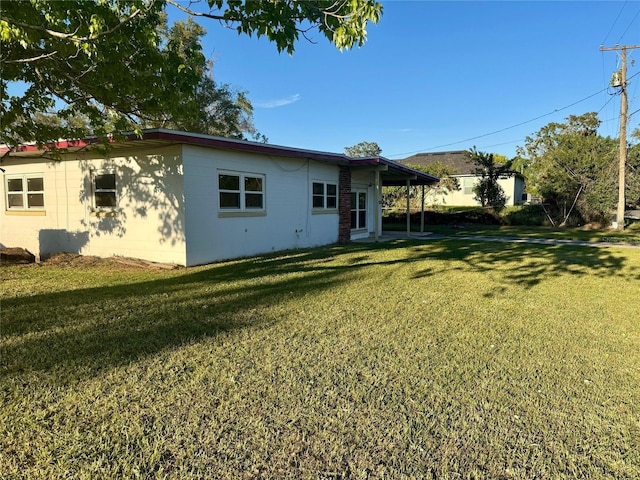 back of house featuring an attached carport, a lawn, and concrete block siding