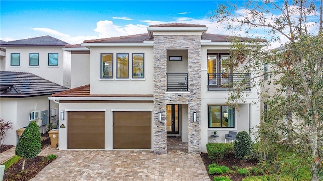 view of front facade with stucco siding, decorative driveway, a balcony, stone siding, and an attached garage