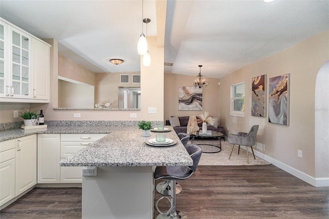 kitchen featuring a breakfast bar, dark wood finished floors, white cabinetry, a peninsula, and glass insert cabinets