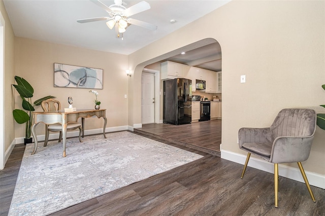 living area with arched walkways, dark wood finished floors, baseboards, and a ceiling fan