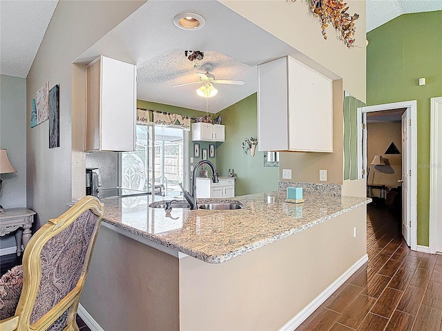 kitchen with a ceiling fan, a sink, a peninsula, lofted ceiling, and wood tiled floor