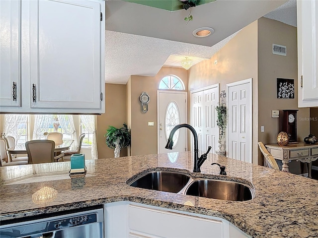 kitchen featuring visible vents, a sink, light stone counters, a textured ceiling, and stainless steel dishwasher