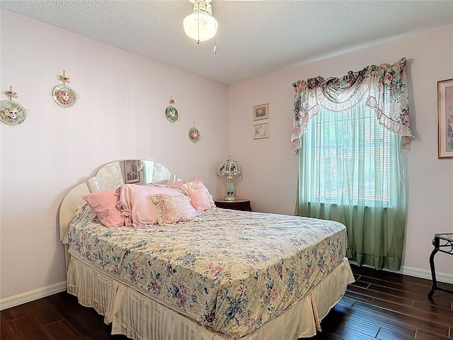 bedroom with a textured ceiling, dark wood-type flooring, and baseboards