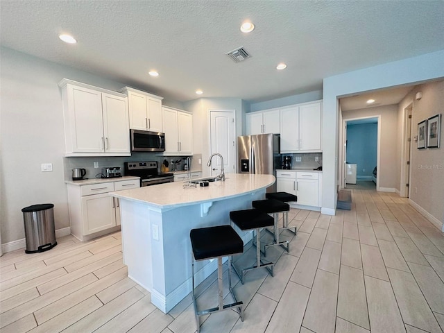 kitchen featuring stainless steel appliances, a breakfast bar, a sink, visible vents, and an island with sink