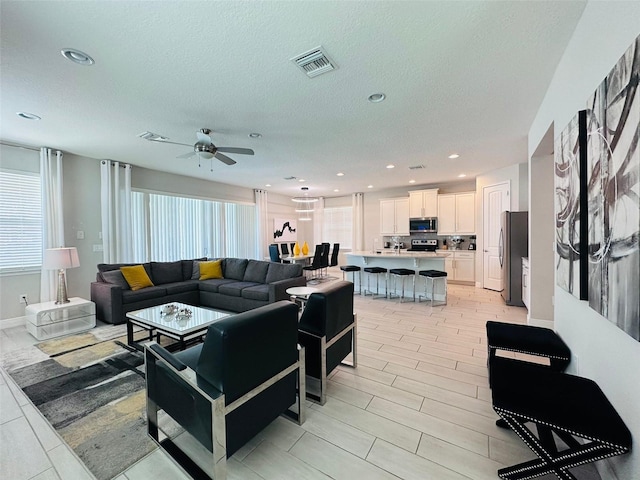 living area featuring ceiling fan, visible vents, a textured ceiling, and recessed lighting