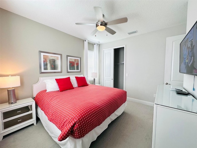 bedroom with a closet, visible vents, light carpet, a textured ceiling, and baseboards