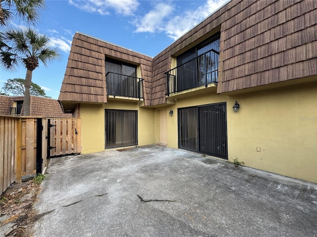 back of property with a garage, mansard roof, a gate, and stucco siding