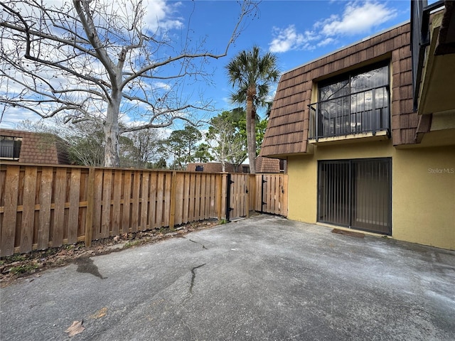 view of home's exterior with a gate, fence, mansard roof, and stucco siding