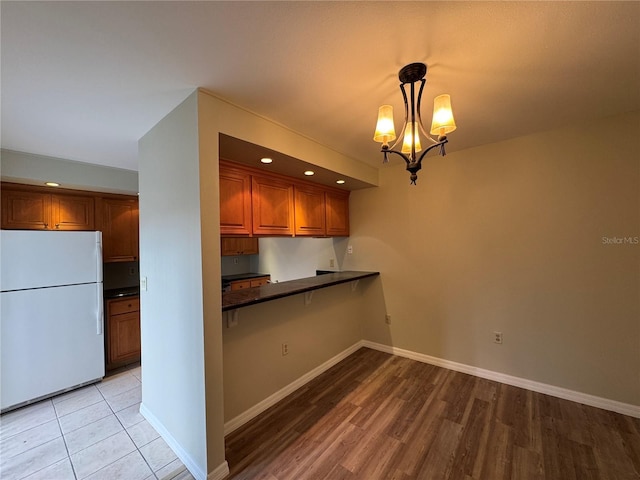 kitchen with dark countertops, an inviting chandelier, brown cabinetry, freestanding refrigerator, and baseboards