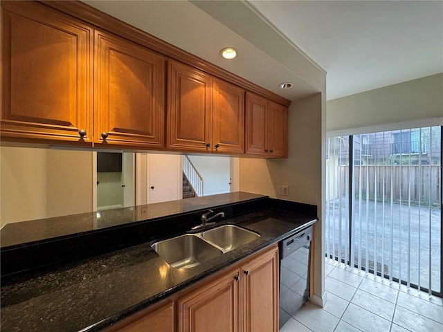 kitchen featuring light tile patterned floors, brown cabinetry, a sink, dark stone countertops, and dishwasher