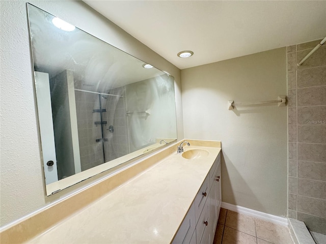 full bath featuring tile patterned flooring, baseboards, tiled shower, and vanity