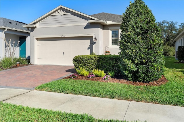 single story home with a front yard, roof with shingles, stucco siding, a garage, and decorative driveway