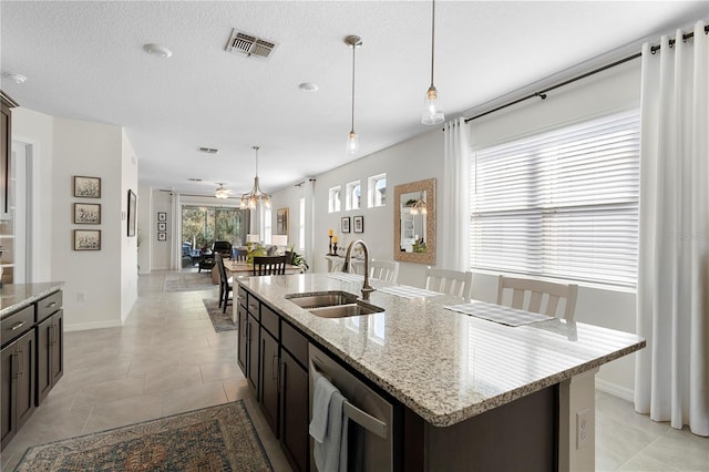 kitchen featuring visible vents, a center island with sink, a sink, stainless steel dishwasher, and hanging light fixtures