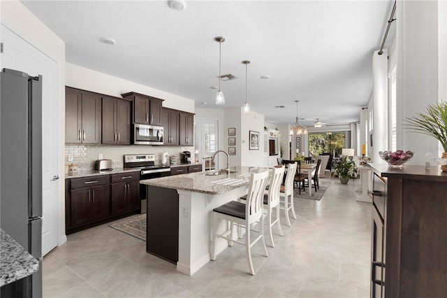 kitchen featuring open floor plan, dark brown cabinets, appliances with stainless steel finishes, and a sink