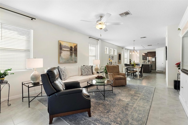 living room featuring light tile patterned flooring, a ceiling fan, visible vents, and baseboards