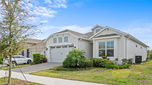 view of front of property with decorative driveway, stucco siding, an attached garage, a front yard, and cooling unit