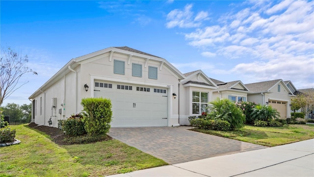 view of front of house with a garage, a front yard, decorative driveway, and stucco siding