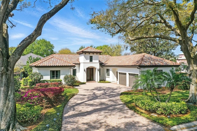 mediterranean / spanish house with decorative driveway, an attached garage, a tile roof, and stucco siding