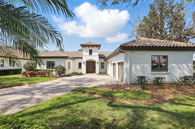 mediterranean / spanish house featuring a garage, a tiled roof, decorative driveway, and a front yard