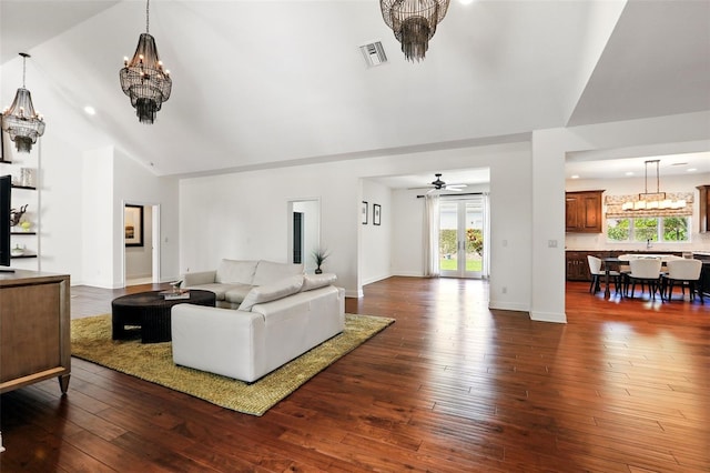 living area with lofted ceiling, visible vents, dark wood-type flooring, baseboards, and ceiling fan with notable chandelier