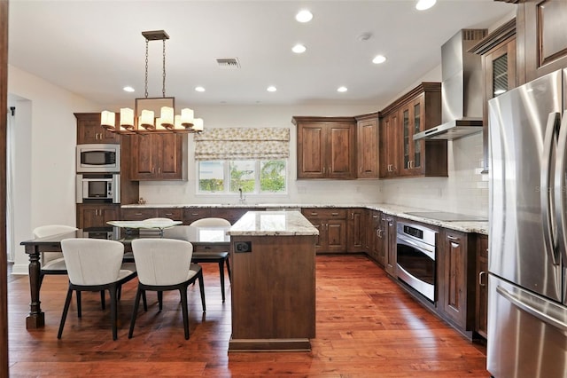 kitchen featuring stainless steel appliances, visible vents, decorative backsplash, wall chimney exhaust hood, and wood-type flooring