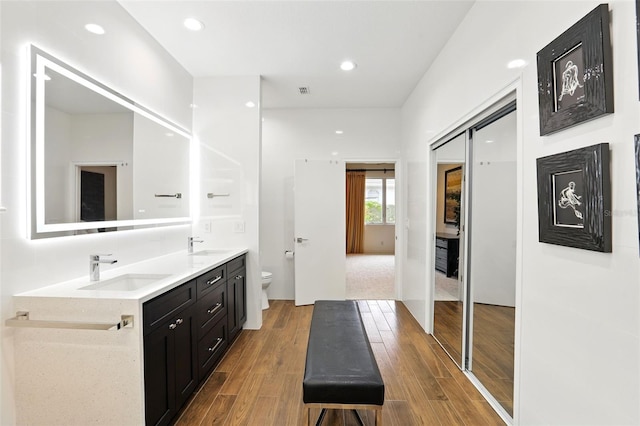 full bath featuring double vanity, wood finished floors, a sink, and toilet