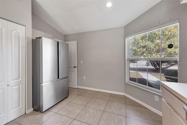 kitchen featuring light tile patterned flooring, freestanding refrigerator, baseboards, and vaulted ceiling