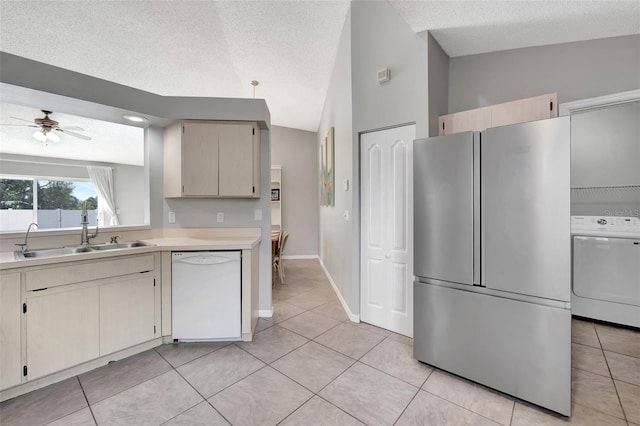 kitchen featuring vaulted ceiling, freestanding refrigerator, white dishwasher, stove, and a sink