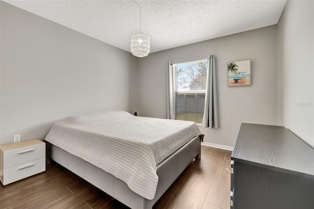 bedroom with an inviting chandelier, dark wood-style floors, baseboards, and a textured ceiling