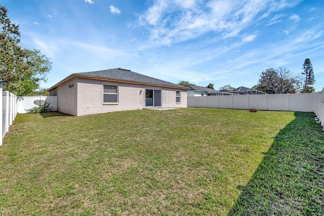 rear view of property with a fenced backyard, a lawn, and stucco siding