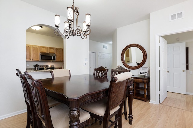 dining space with light wood finished floors, visible vents, arched walkways, and baseboards