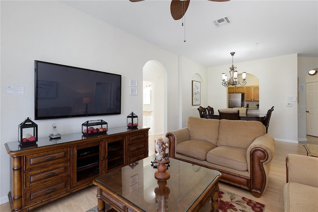 living area with baseboards, visible vents, light wood-style flooring, arched walkways, and ceiling fan with notable chandelier