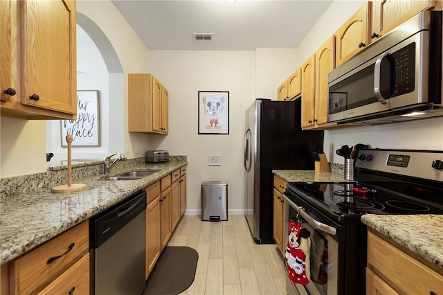 kitchen featuring light stone counters, visible vents, a sink, stainless steel appliances, and light wood-style floors