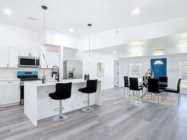 kitchen featuring light wood finished floors, tasteful backsplash, a center island with sink, appliances with stainless steel finishes, and light countertops