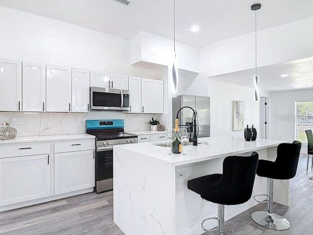 kitchen featuring pendant lighting, backsplash, appliances with stainless steel finishes, a sink, and an island with sink