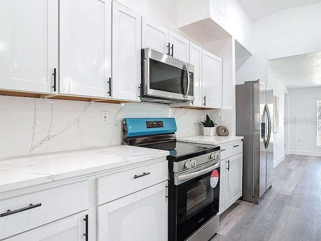 kitchen featuring light wood finished floors, tasteful backsplash, appliances with stainless steel finishes, light stone counters, and white cabinetry