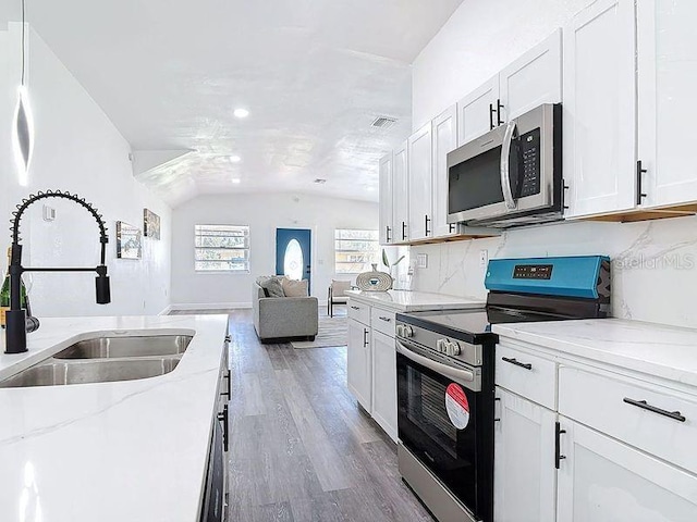 kitchen featuring stainless steel appliances, wood finished floors, a sink, open floor plan, and vaulted ceiling