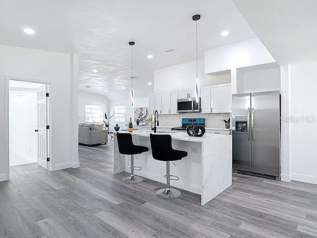 kitchen with appliances with stainless steel finishes, light countertops, an island with sink, and wood finished floors